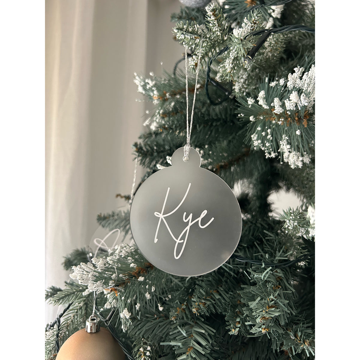 Frosted Bauble personalised with a short name in white script, close-up on a snowy tree